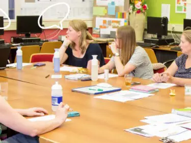 Een groep mensen die aan een tafel zit, actief deelneemt aan een gesprek en vragen stelt, terwijl hun discussie geanimeerd en levendig wordt. School en Veiligheid