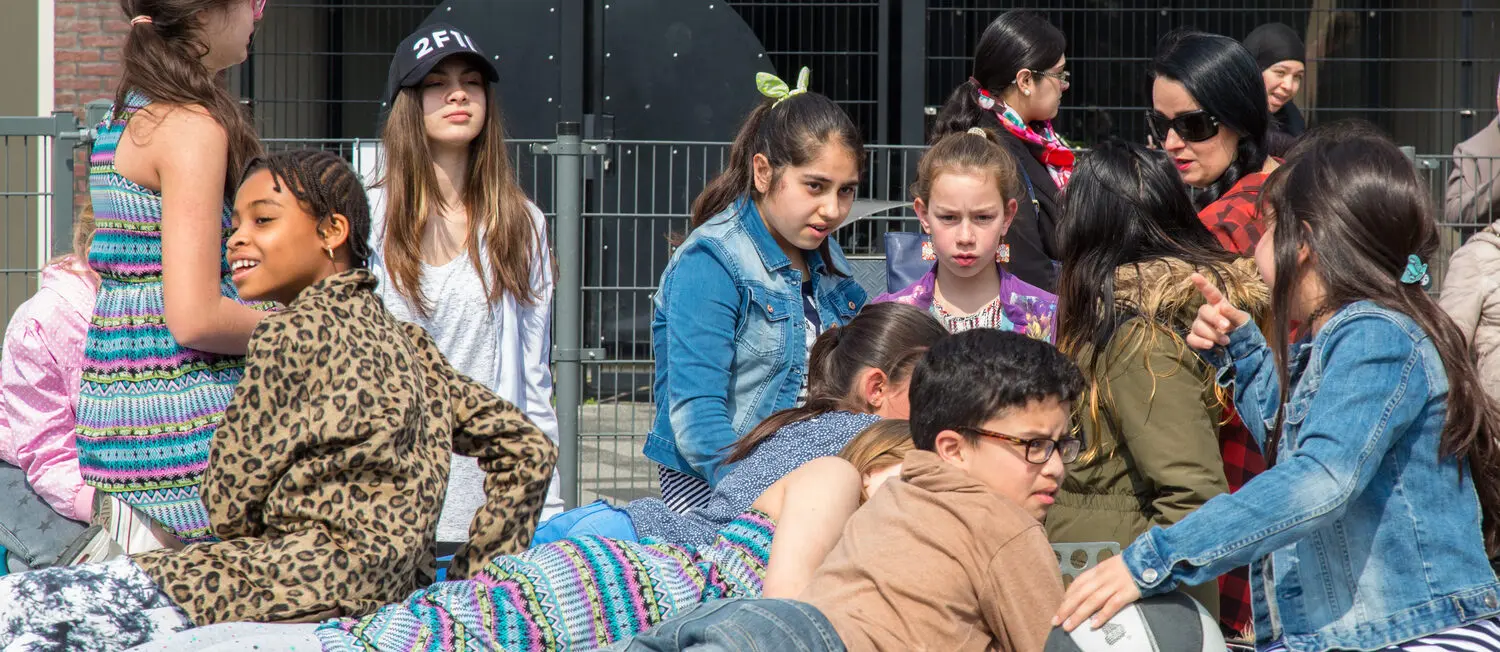 Beschrijving: Een groep kinderen die op een bank voor een hek zitten. School en Veiligheid