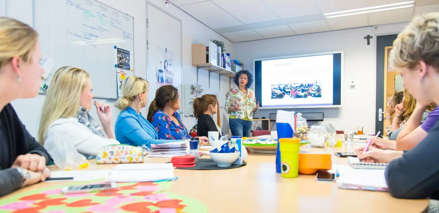 Een groep trainers en gastdocenten zit rond een tafel in een klaslokaal. School en Veiligheid