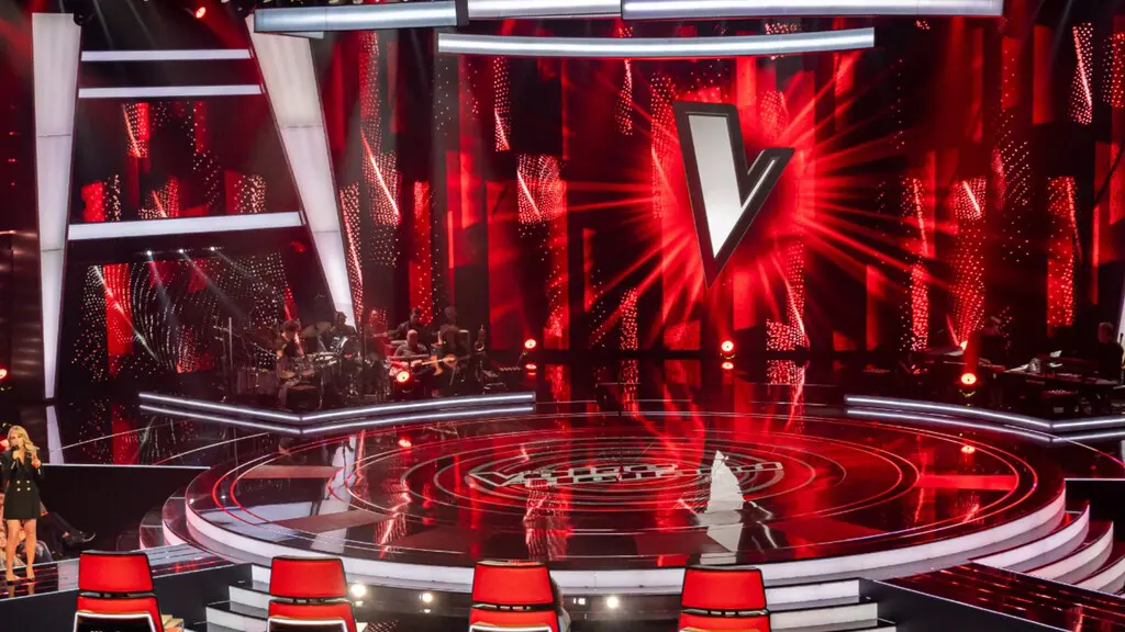 Een podium met rode lichten en een podium ervoor waar studenten na The Voice een gesprek voeren over seksueel wangedrag. School en Veiligheid