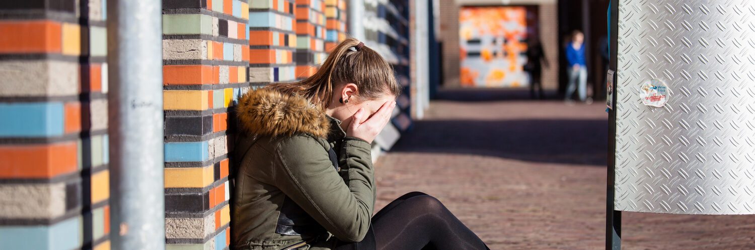 Een vrouw zit op een bakstenen muur naast een vuilnisbak met posters in de buurt. School en Veiligheid