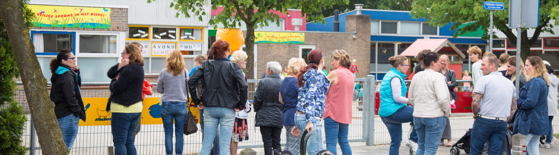 Een groep mensen, inclusief ouders (Ouderavond), staat in de rij voor een winkel en voert een gesprek over pesten. School en Veiligheid