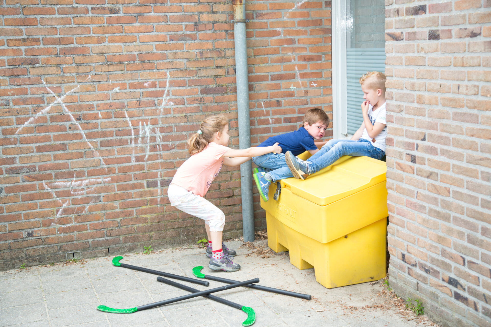 Beschrijving: Een groep kinderen die met een skateboard spelen voor een houten muur, waar ze zich veilig voelen op het schoolplein. School en Veiligheid