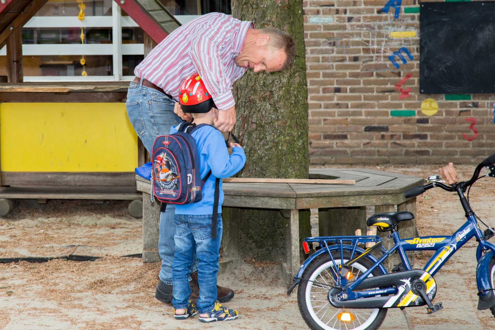 Een man helpt een jongen met zijn fiets tijdens een buitenactiviteit. School en Veiligheid