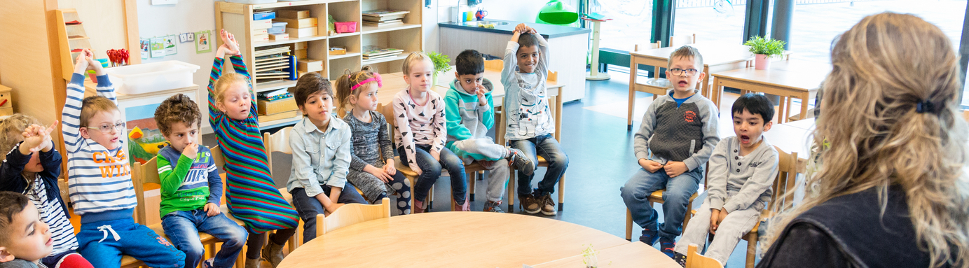 Een groep kinderen die in een klaslokaal rond een tafel zitten en een Talking Stick doorgeven. School en Veiligheid