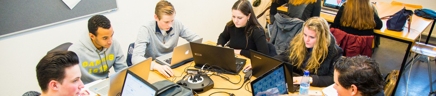 Een groep mensen, met name studenten en medewerkers, die op laptops werken in een kamer op de school als plek van ontmoeting. School en Veiligheid