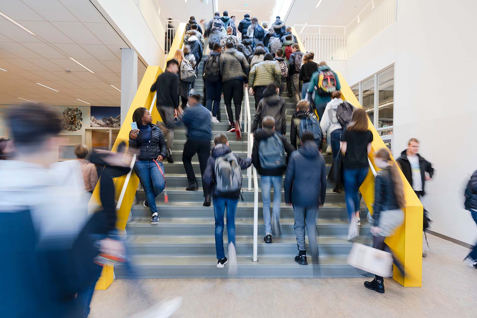 Een groep mensen die de trap oploopt in een school, waar het gevoel van een schoolgemeenschap en gedeelde waarden zwaarder weegt dan elke mogelijkheid van criminele activiteiten. School en Veiligheid